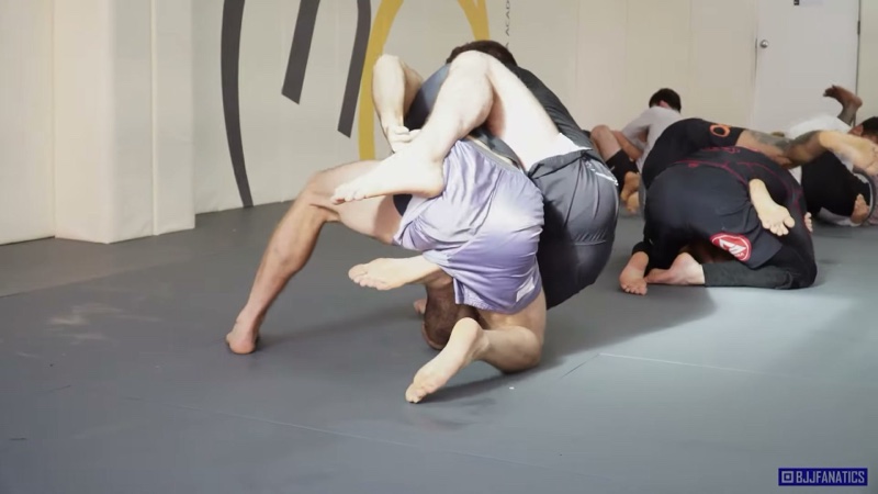 Two no-gi grapplers scramble in the foreground while other pairs roll in the same academy.