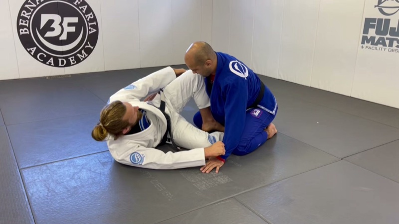 A seated guard player hooks both feet inside the kneeling opponent's thighs in butterfly guard.