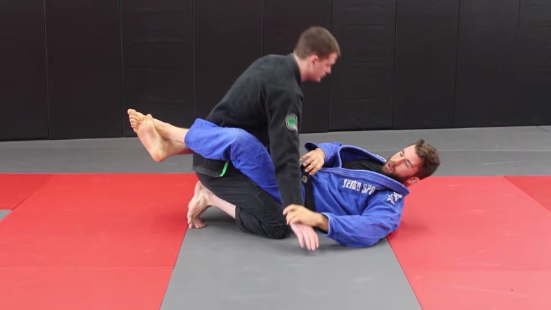 The bottom player in a blue gi locks both legs around the kneeling opponent's waist in closed guard.