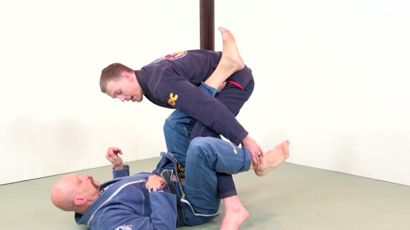 A standing passer stacks the bottom player's legs to one side while passing open guard.