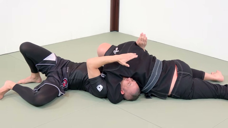 The top player lies chest-down over the bottom player's head, heads pointing opposite ways, in north-south.
