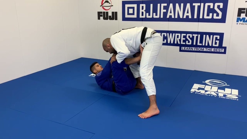 The bottom player in a blue gi frames a standing opponent with both legs from open guard.