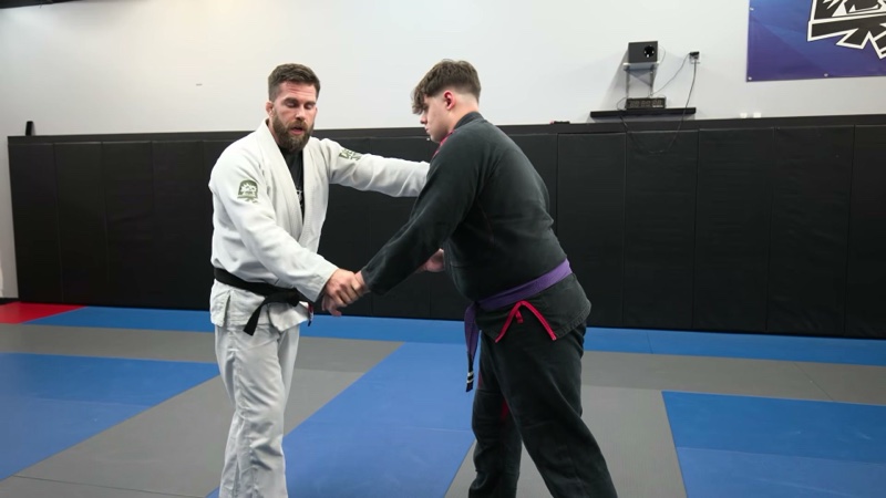 Two grapplers stand face to face on the mats, one holding a collar grip and a sleeve grip.